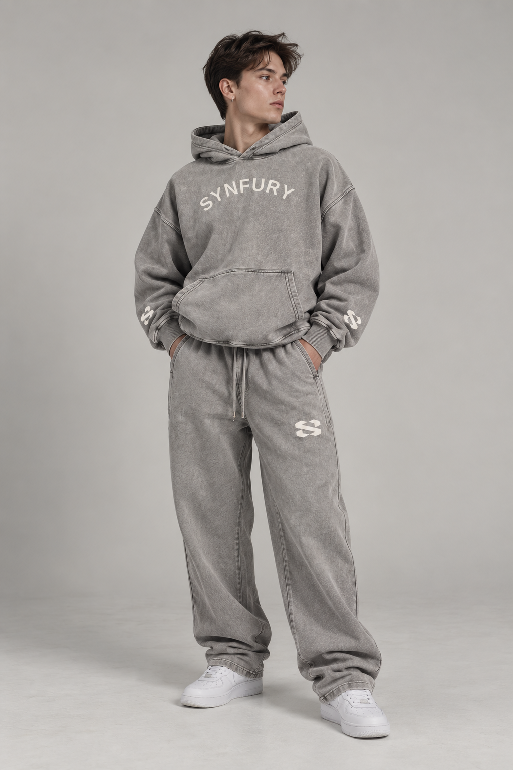 The Core Collection Set worn on model — Fog Gray heavyweight cotton hoodie and matching sweatpants, snow-wash finish, SYNFURY word mark and 'S' logo, styled with white sneaker