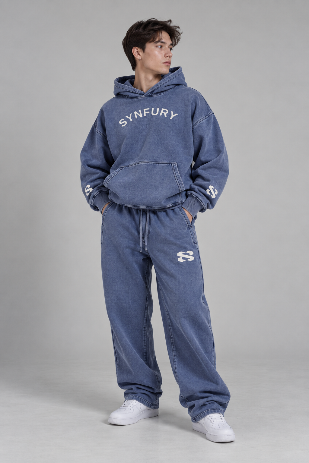 The Core Collection Set worn on model — Storm Navy heavyweight cotton hoodie and matching sweatpants, snow-wash finish, SYNFURY word mark and 'S' logo, styled with white sneakers