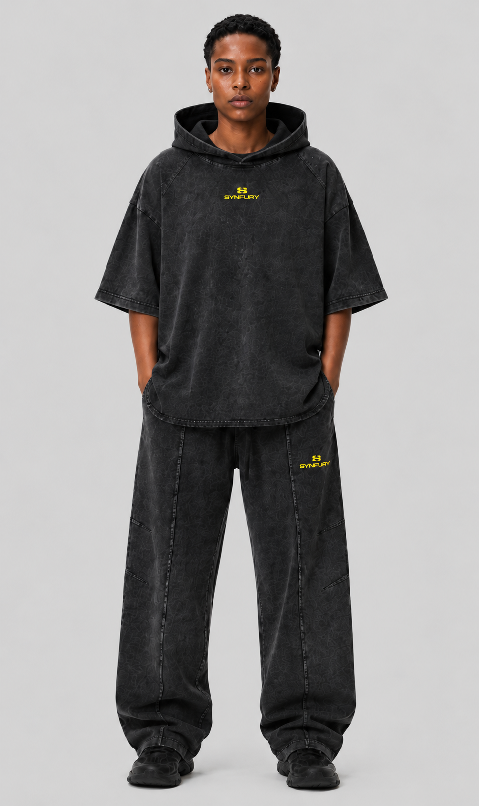 "Curved Panel Raglan Hoodie and matching sweatpants worn on model — Cinder Black heavyweight cotton, half-sleeve raglan fit, yellow SYNFURY logo on chest and thigh"