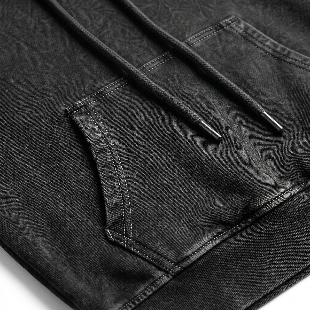 Close-up of a black washed denim hoodie showing the front kangaroo pocket, detailed stitching, and a black drawstring with a metal tip.