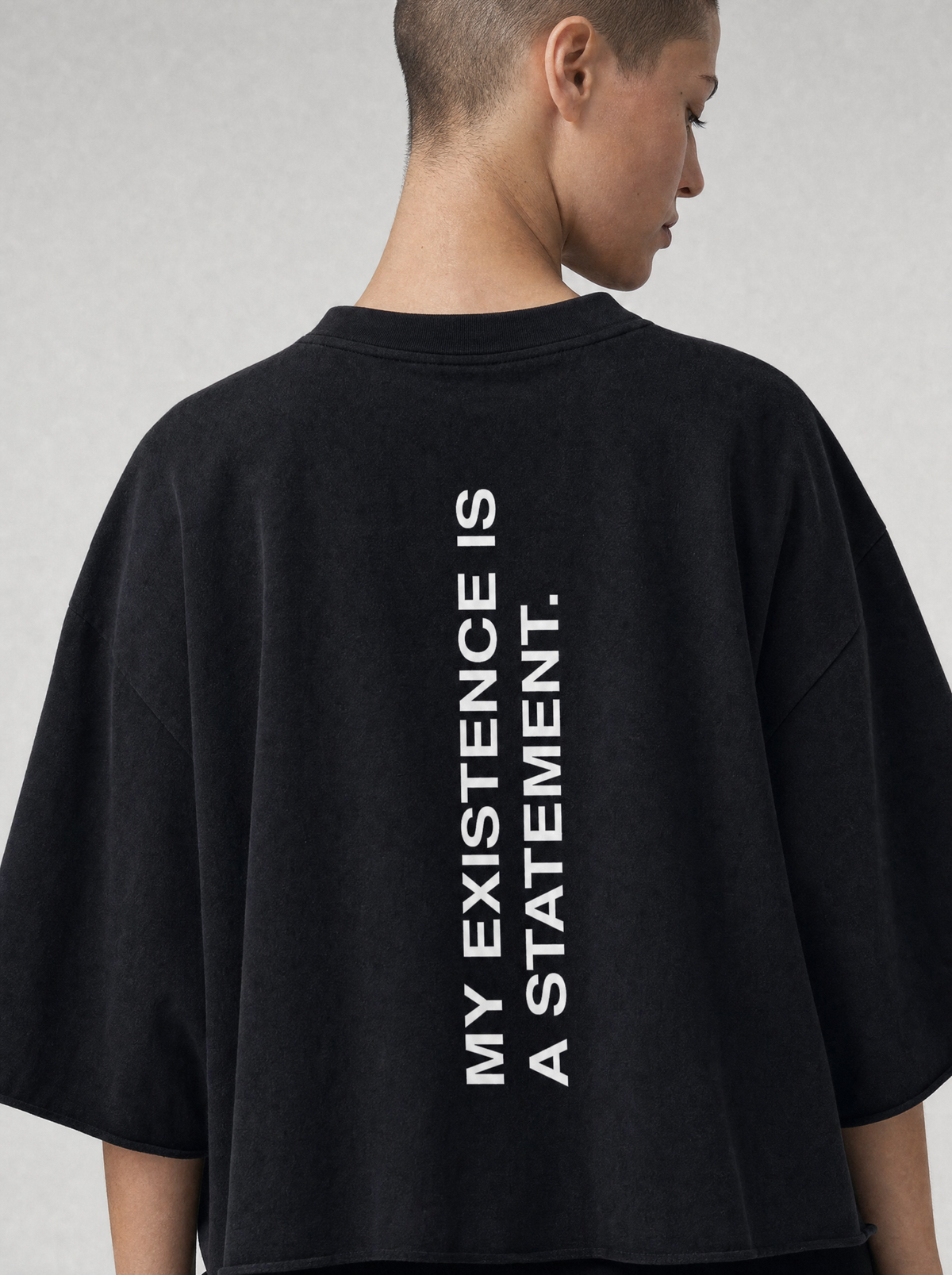 The Statement Tee in Black, back view — heavyweight cotton, oversized fit, bold vertical print reading 'My existence is a statement