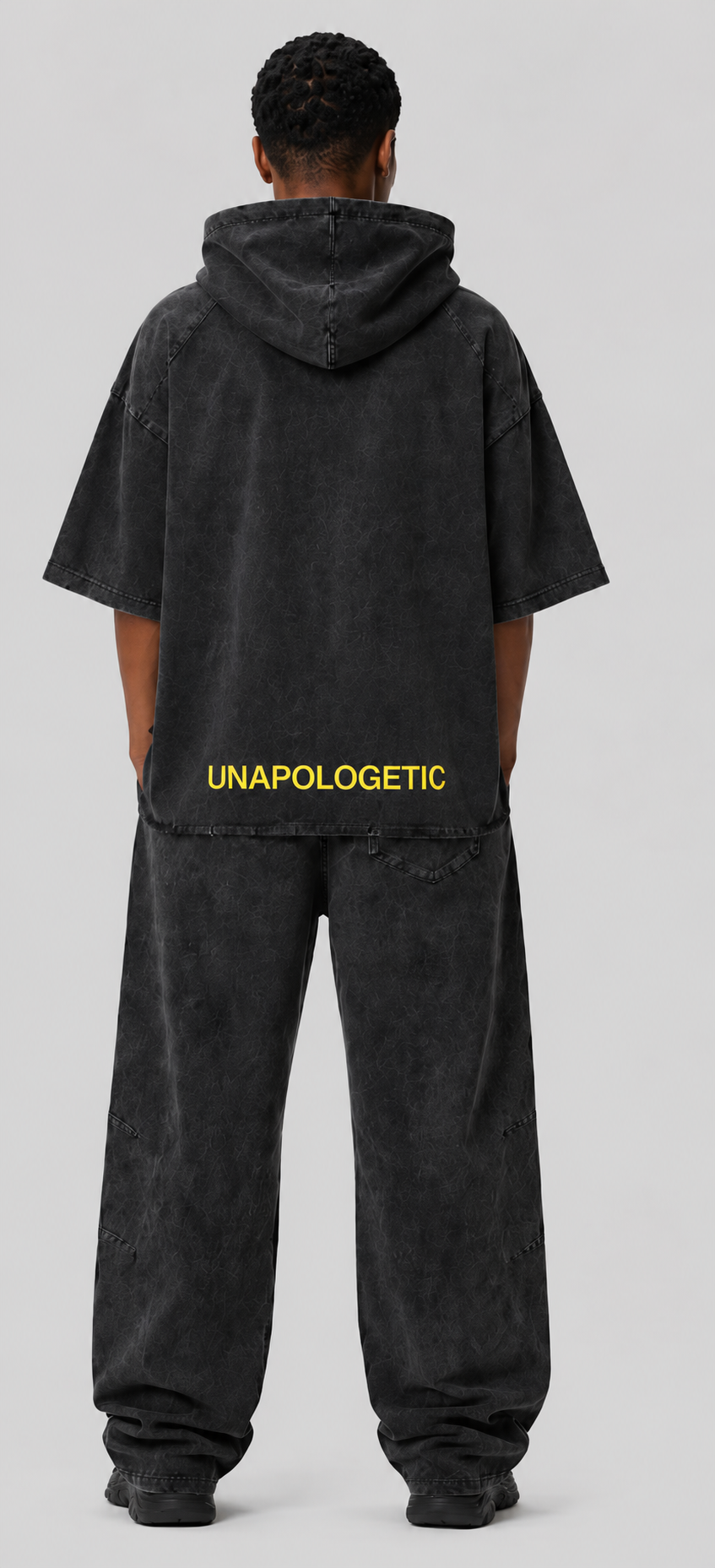 "The Unapologetic Hooded Set worn on model, back view — heavyweight cotton half-sleeve hoodie and matching sweatpants, yellow 'UNAPOLOGETIC' print across back"
