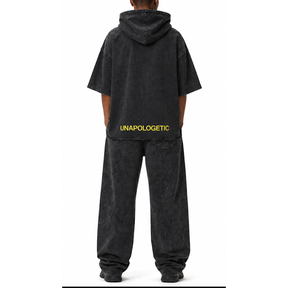 Model shown from the back wearing a matching SYNFURY Cinder Black hooded sweatshirt and wide-leg trail sweatpants set. The hoodie has 'UNAPOLOGETIC' printed in yellow across the lower back.