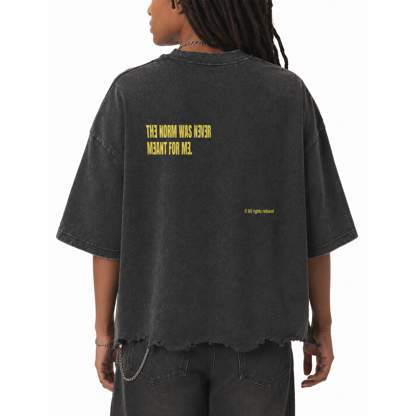 A person shown from the back wearing an oversized faded black graphic T-shirt with yellow text reading 'THIS NORM WAS NEVER MEANT FOR ME.' and a small copyright line near the lower back.