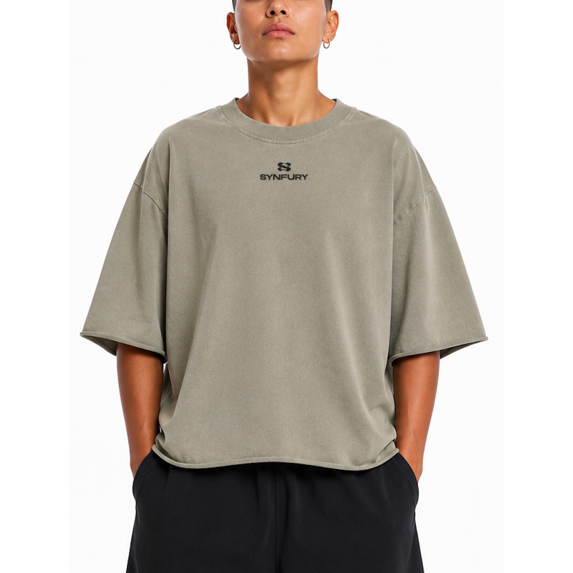 A model wearing an oversized short-sleeve t-shirt in a muted sage green color with a black 'SYNFURY' logo printed on the chest, paired with black pants against a plain white background.