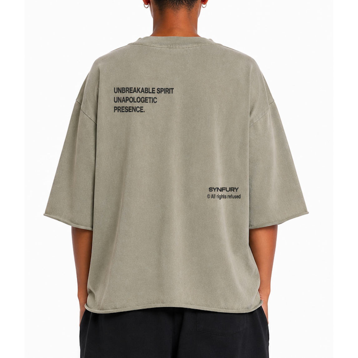 SYNFURY model wearing an oversized Khaki T-shirt with black printed text on the upper back and lower right back, paired with dark pants against a plain white studio background.