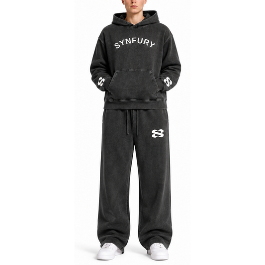 A model wearing a matching black washed hoodie and sweatpants set with white graphic details, including the brand name 'SYNFURY' on the chest and a stylized 'S' logo on the thigh.